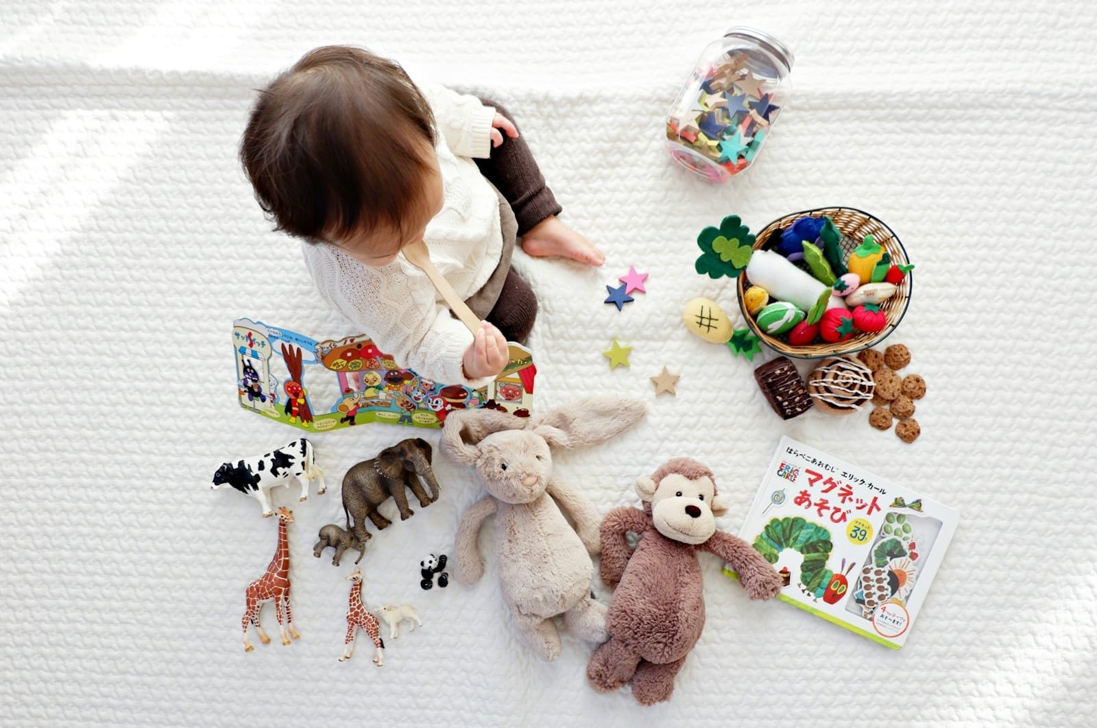 Photo by Yuri Li boy sitting on white cloth surrounded by toys